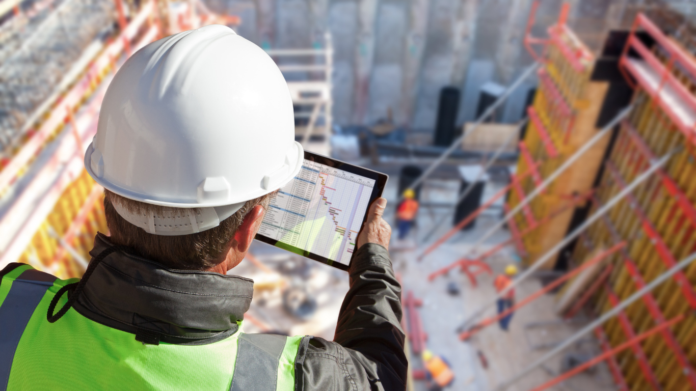 A construction worker is looking at a tablet at a construction site.