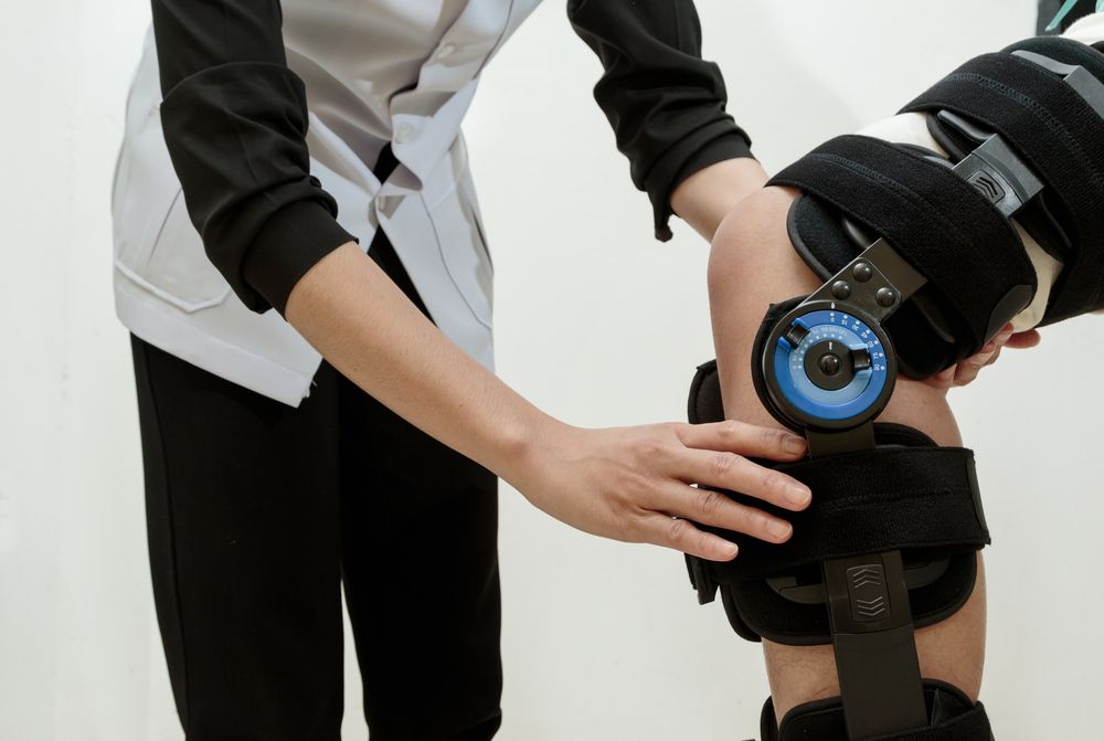Person adjusting knee brace on patient's leg. Black brace with blue dial. — Bourbong Street Physiotherapy Centre in Bundaberg West, QLD