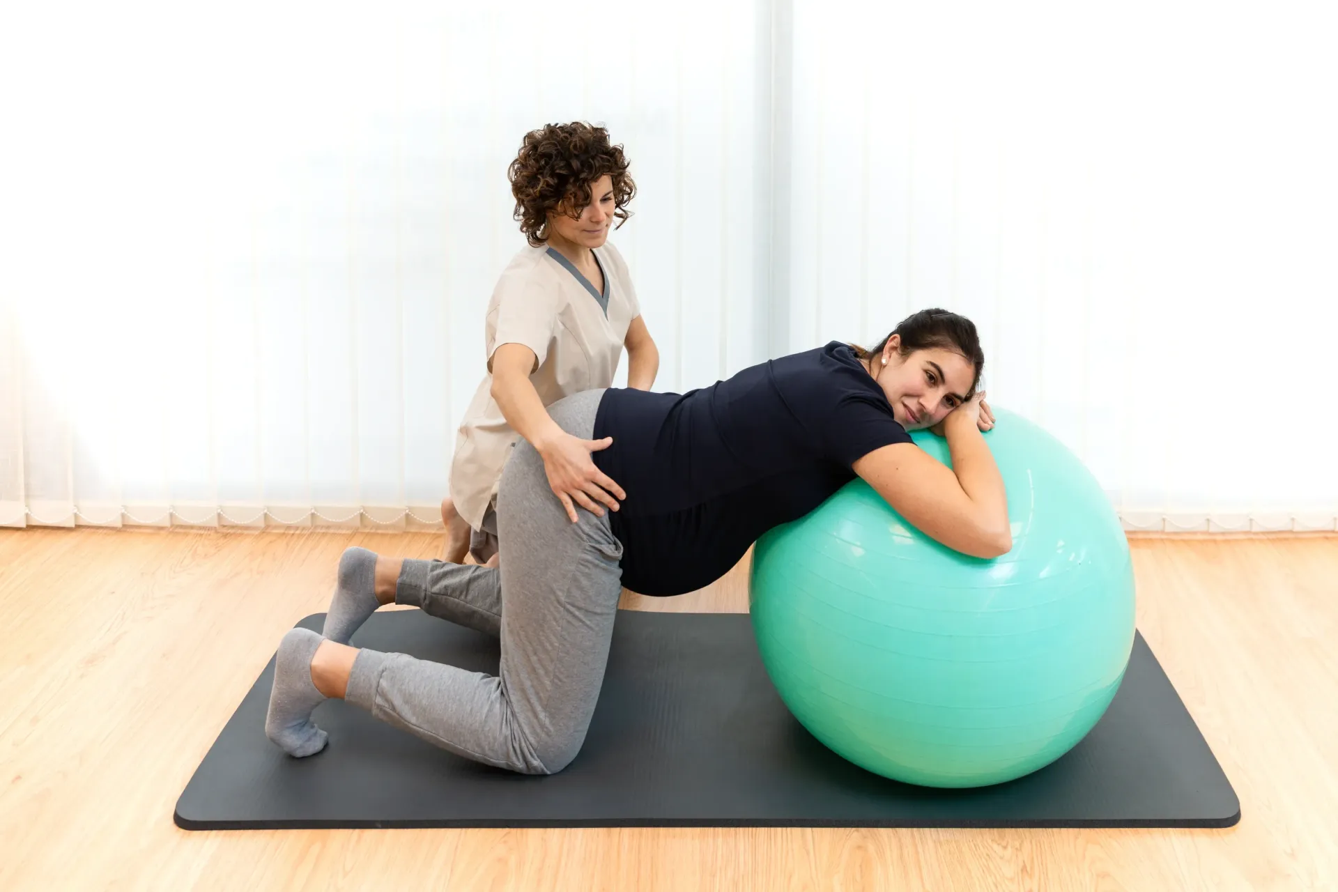 Pregnant woman on exercise ball, assisted by a therapist, on a mat. Interior. — Bourbong Street Physiotherapy Centre in Bundaberg West, QLD