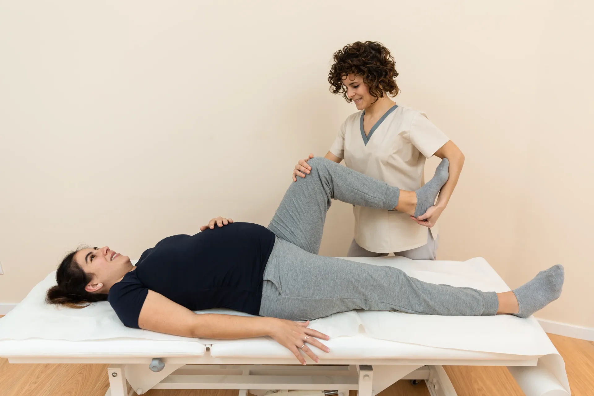 Pregnant person receiving physical therapy on a treatment table. Therapist stretches their leg. Neutral setting. — Bourbong Street Physiotherapy Centre in Bundaberg West, QLD