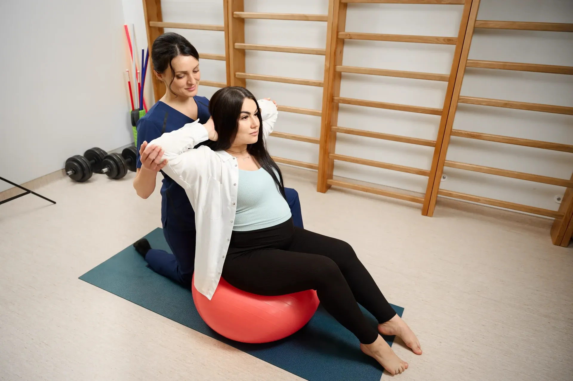 Woman on exercise ball, assisted by a person in a blue uniform, stretching her arm in a gym. — Bourbong Street Physiotherapy Centre in Bundaberg West, QLD