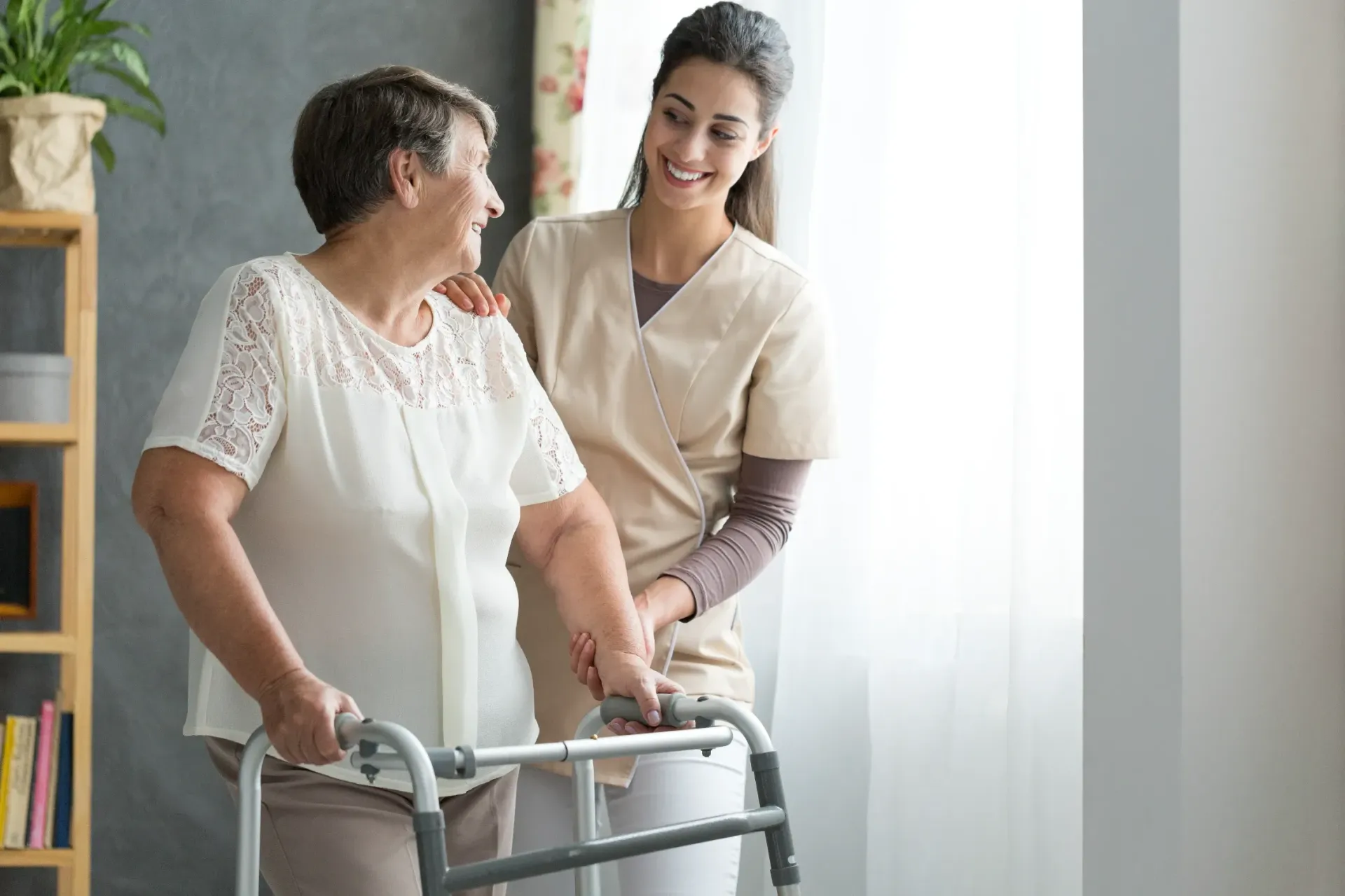 Woman using a walker with assistance from a smiling caregiver in a home setting. — Bourbong Street Physiotherapy Centre in Bundaberg West, QLD