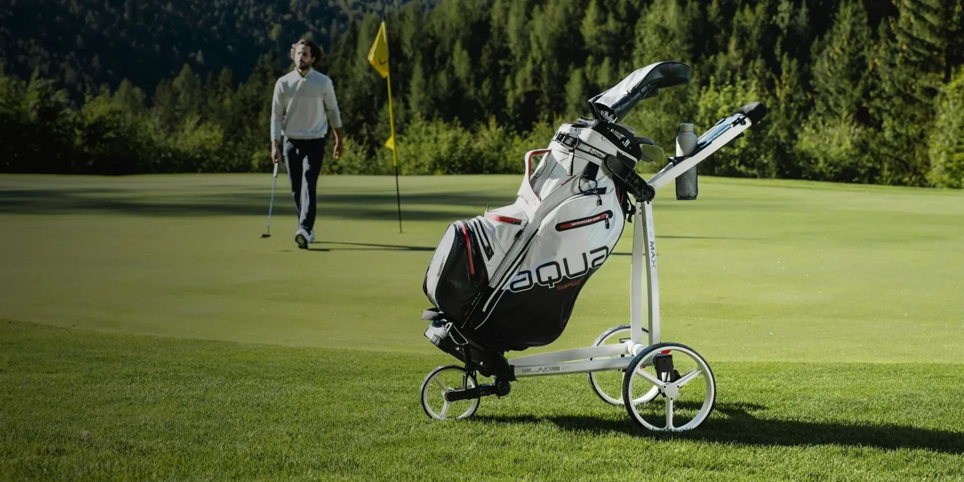 A man is walking on a golf course with a golf bag on a cart.