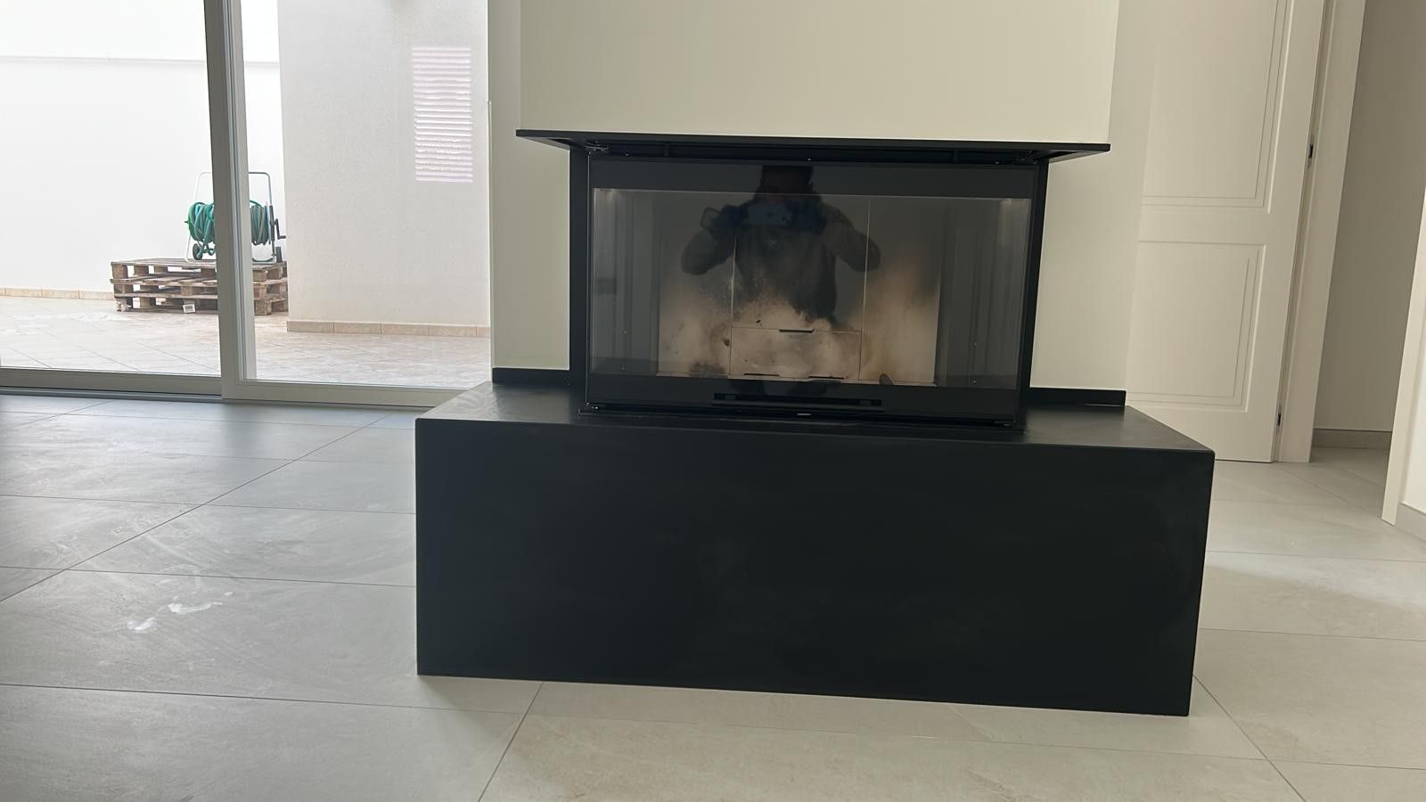 In una stanza moderna e luminosa, un inserto per camino nero poggia su una base rettangolare nera, addossato a una parete bianca.