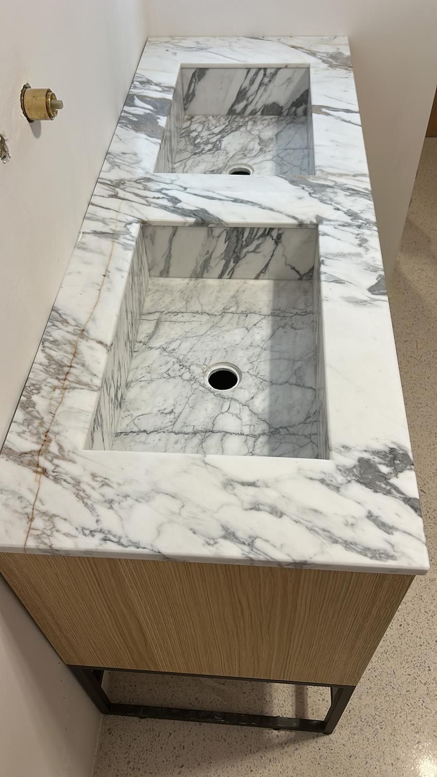Doppio lavabo con piano in marmo bianco e grigio, lavabi integrati e mobili in legno chiaro su base metallica.