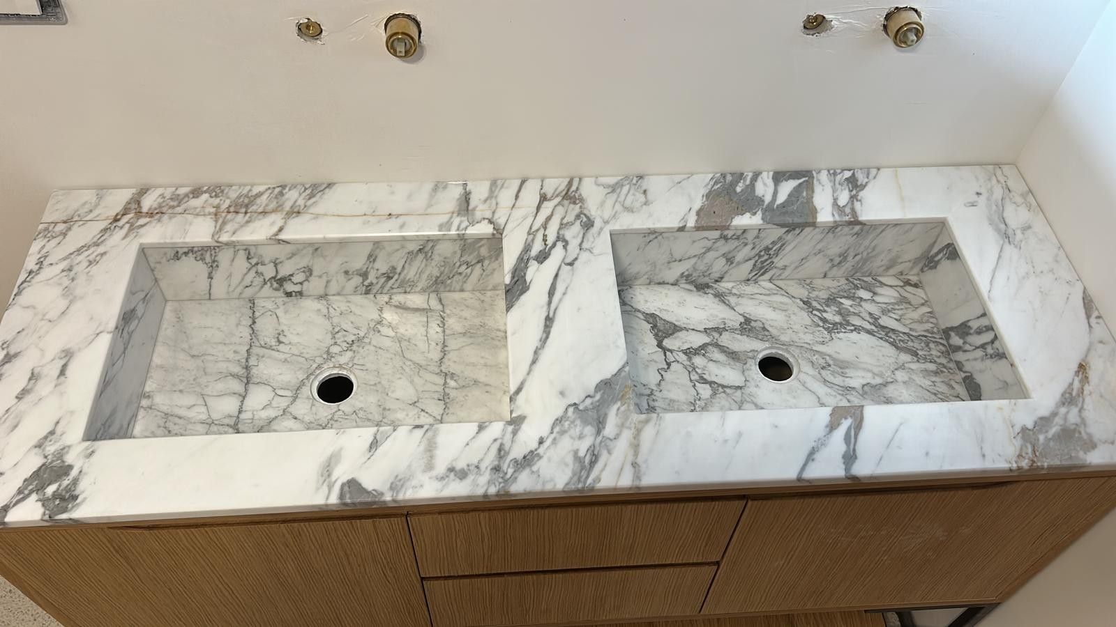 Vista dall'alto di un mobile bagno con doppio lavabo in marmo, lavabi integrati e rubinetti a parete color oro.