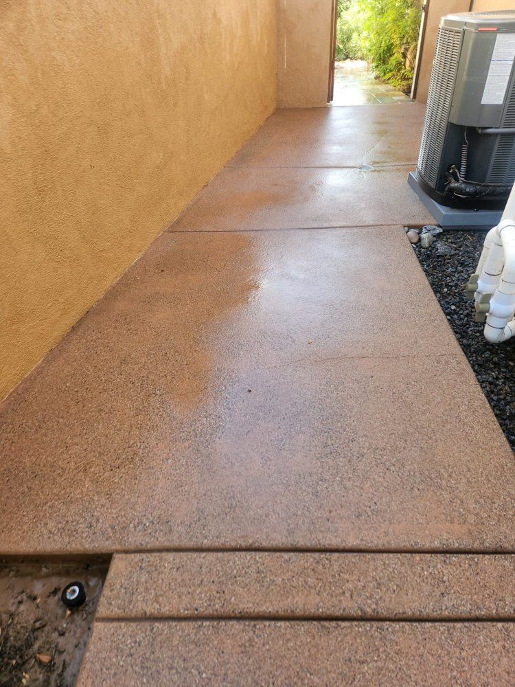 A concrete walkway next to a wall with an air conditioner on it.