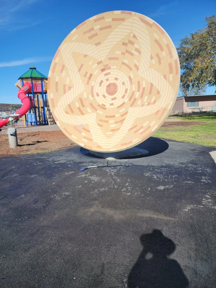 A large circular object in a park with a playground in the background