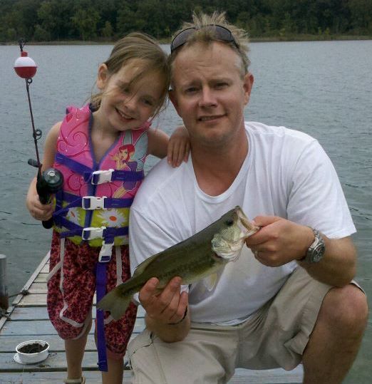 A man and a little girl on a dock holding a fish