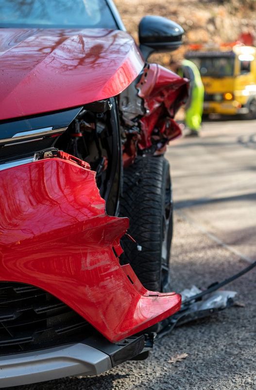 A red car with a damaged bumper is parked on the side of the road.