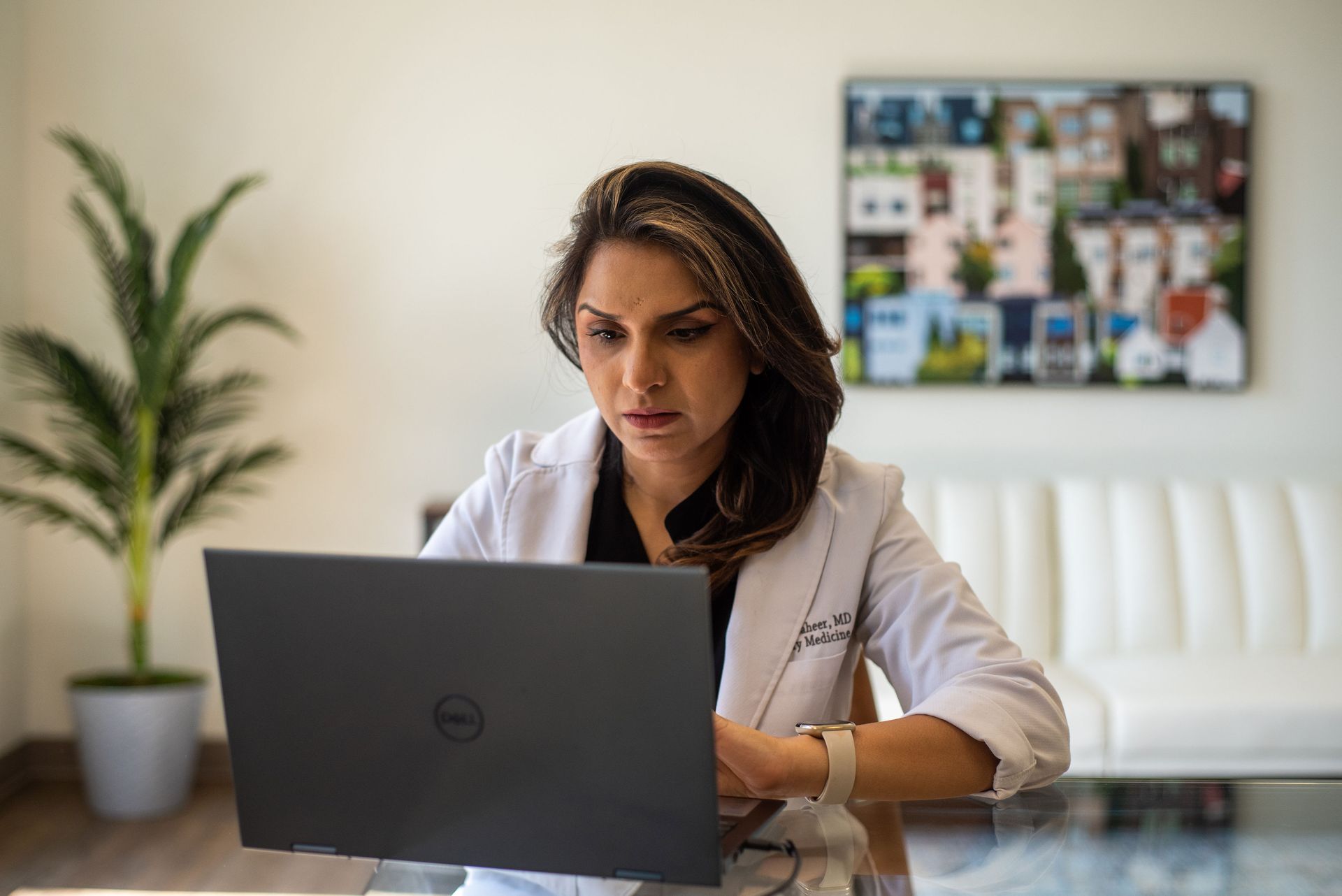 A woman in a lab coat is sitting at a table using a laptop computer.