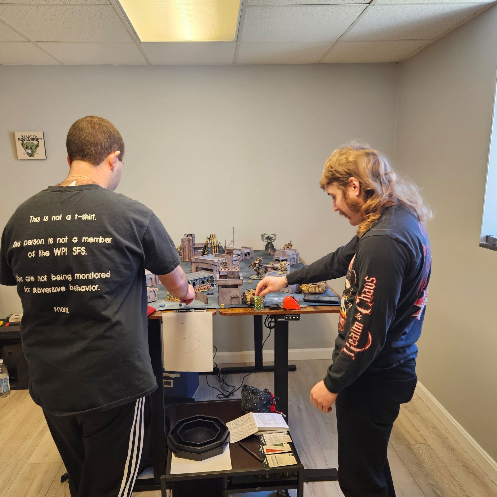 Two men standing in a room with one wearing a t-shirt that says texas chainsaws