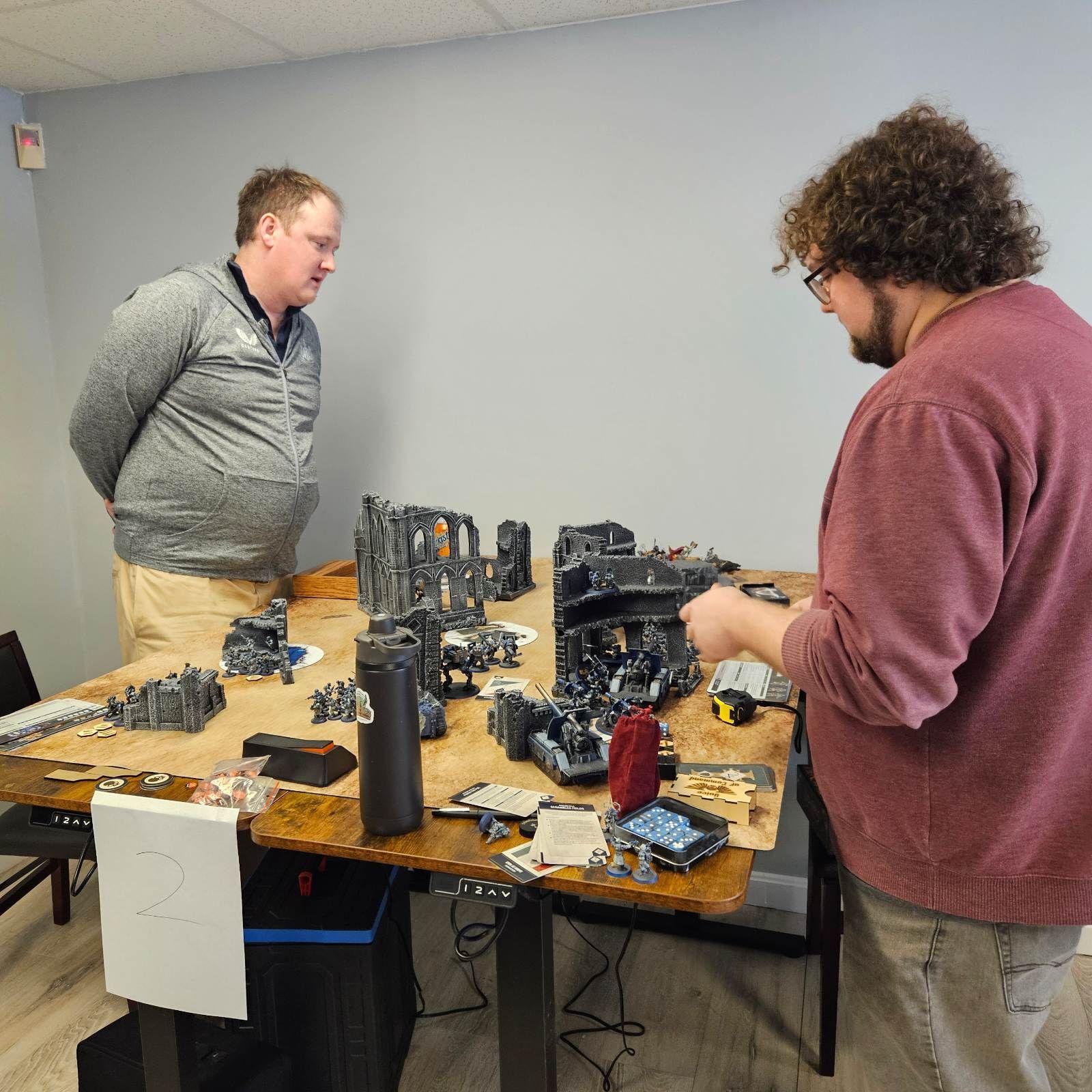 Two men are standing around a table with a lot of toys on it