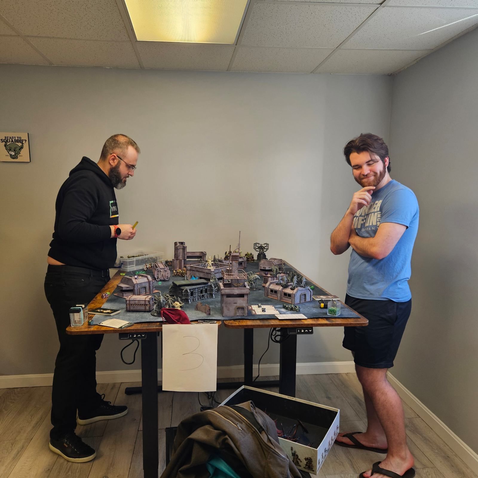Two men are standing in front of a table with miniature buildings on it
