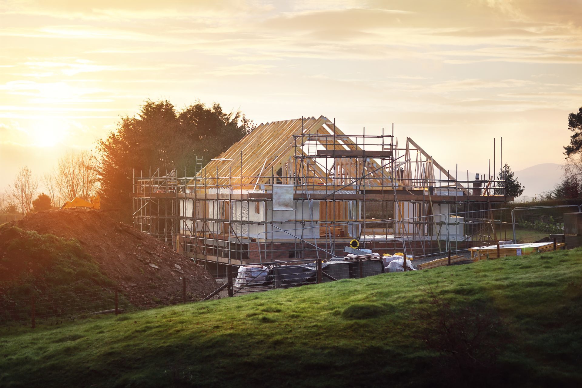 A house is being built in a field with a sunset in the background.