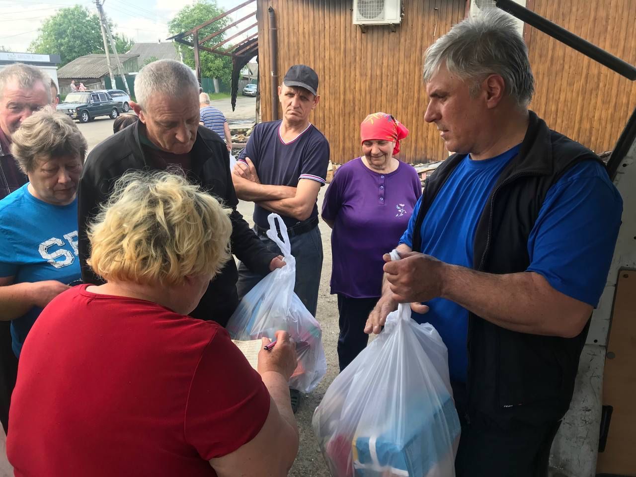 A group of people receiving food and essentials in white carrier bags.