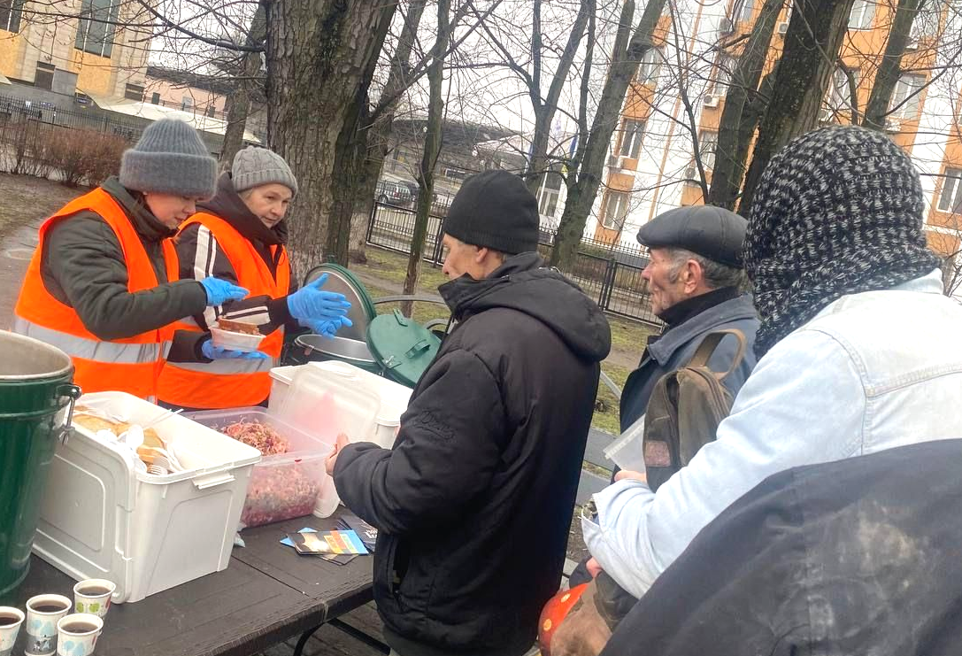 People in high-Vis jackets and hats handing out food to people queuing.