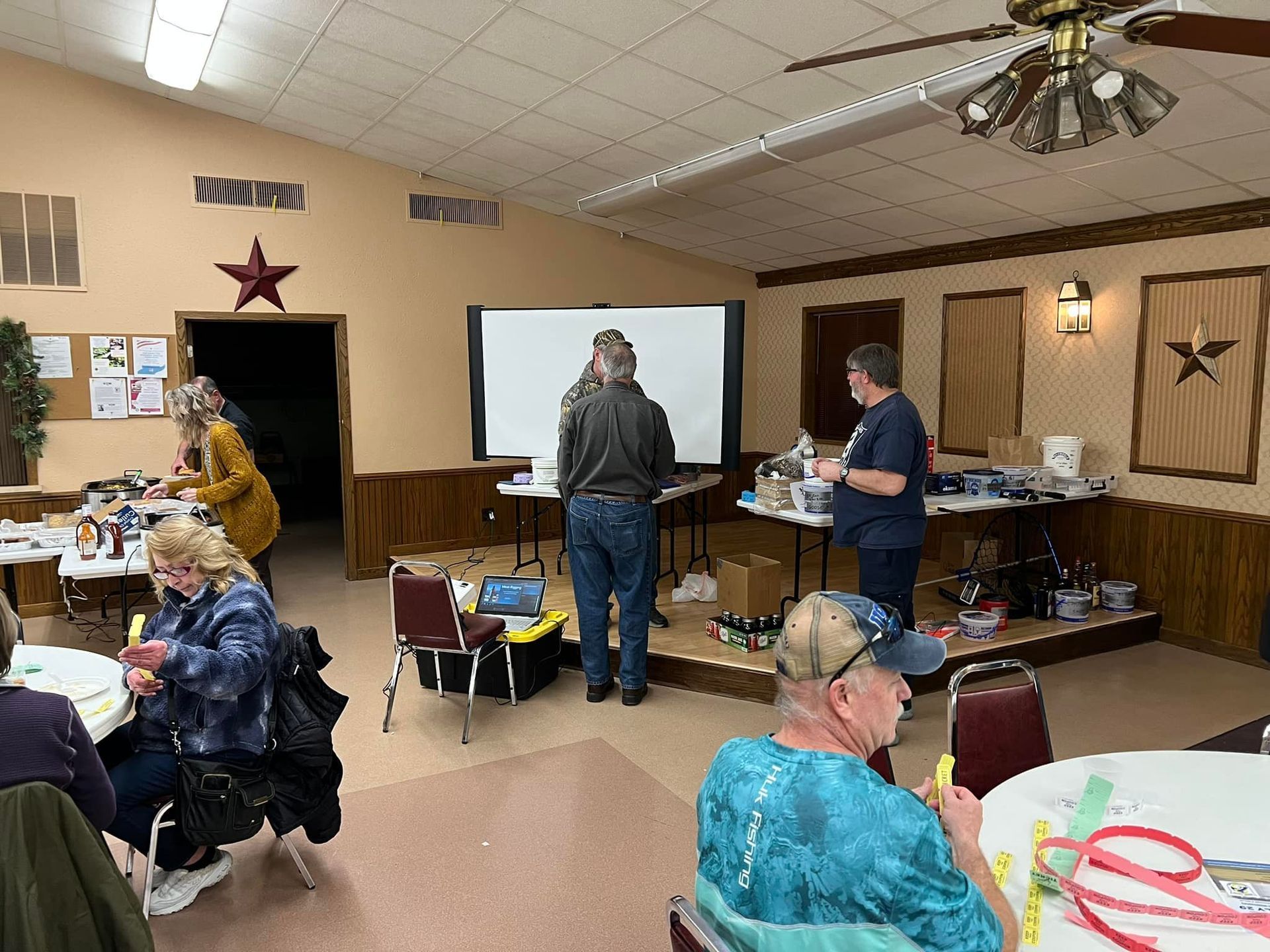 A group of people are sitting at tables in a room with a projector screen.