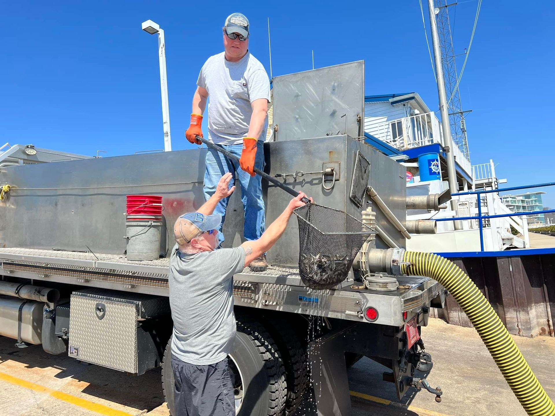 Two men are working on a large truck with a hose attached to it.