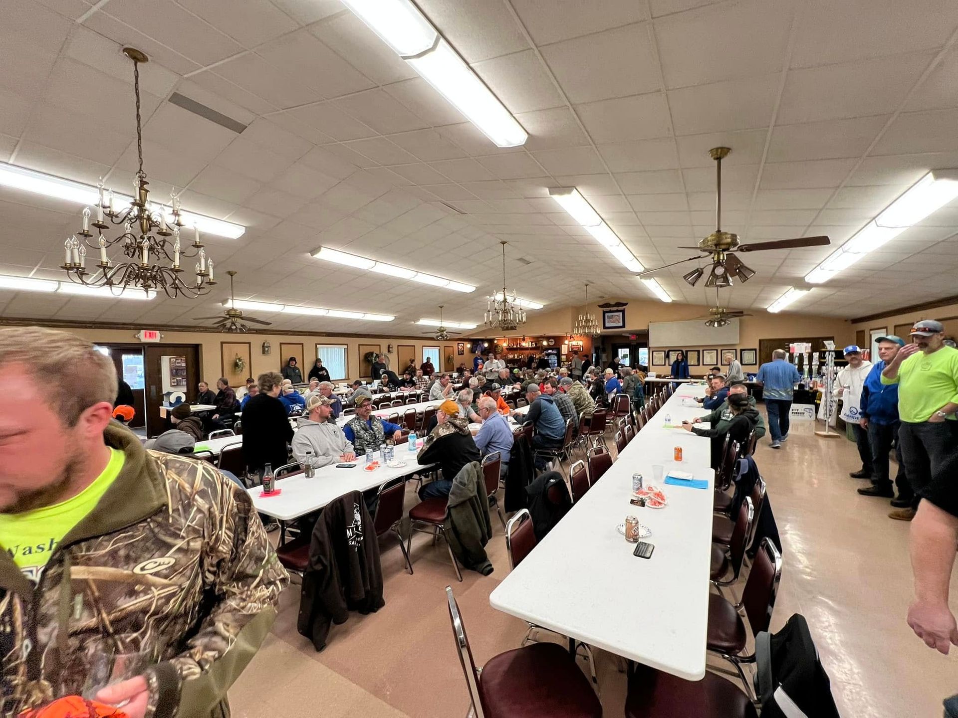 A group of people are sitting at long tables in a large room.