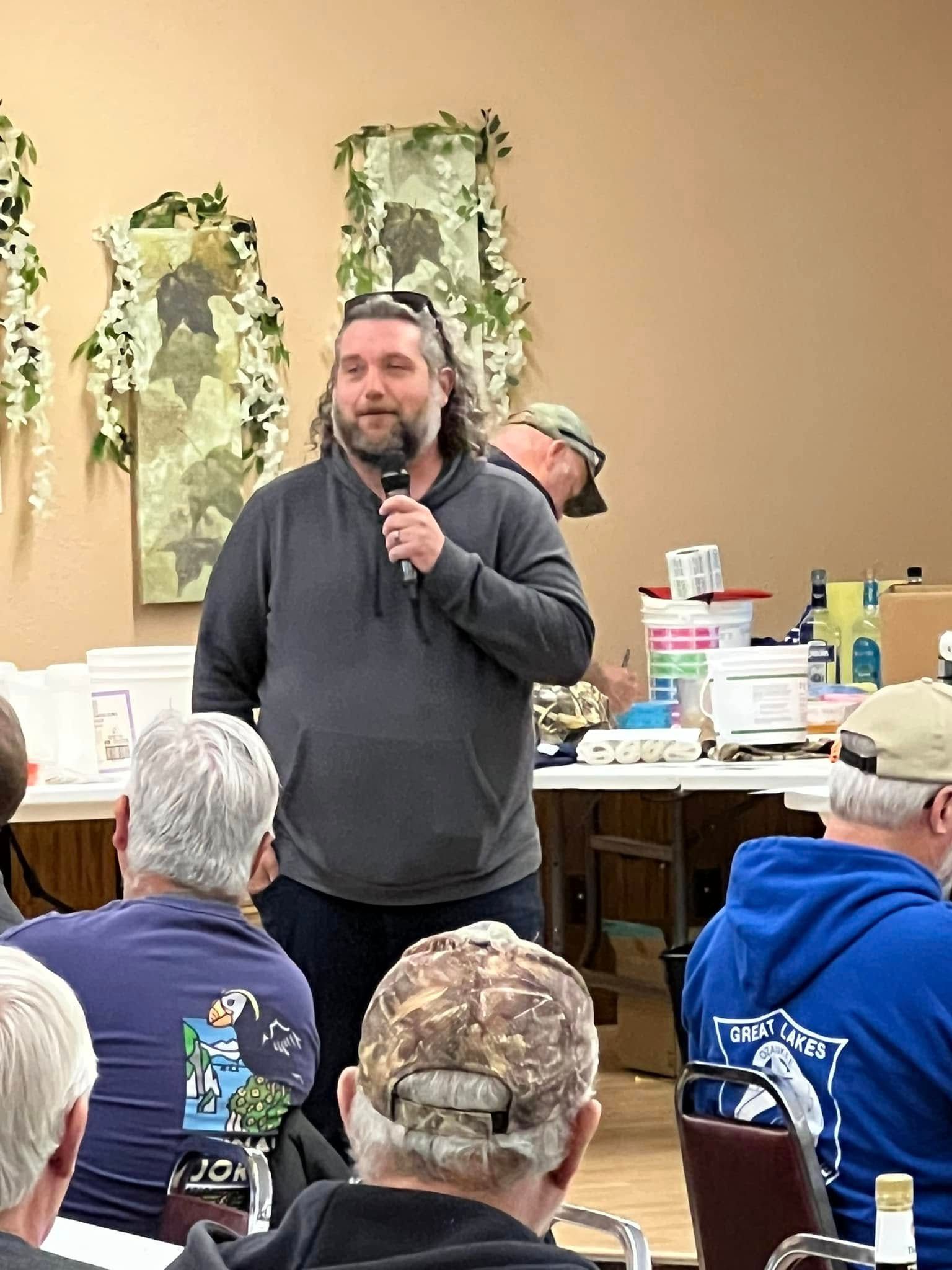 A man is standing in front of a group of people holding a microphone.