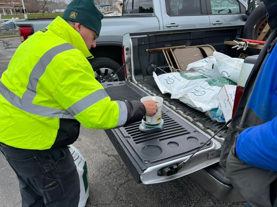 A man in a yellow jacket is cleaning the back of a truck.