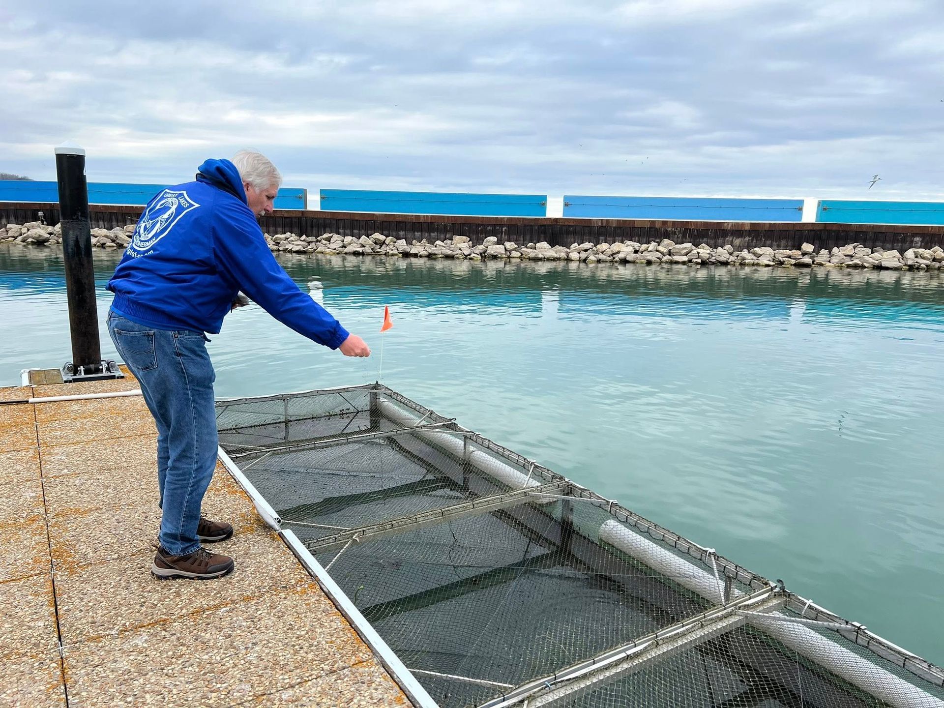 A man in a blue hoodie is standing on a dock near a body of water.