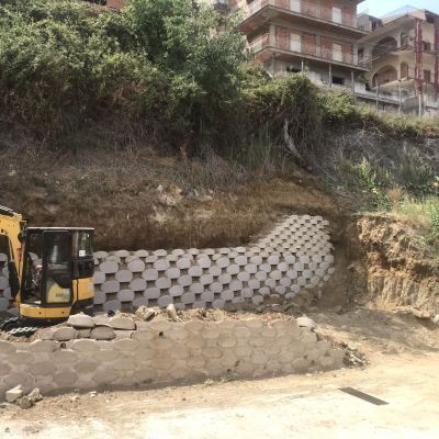 Un escavatore giallo sta percorrendo una strada sterrata accanto a un muro di cemento.