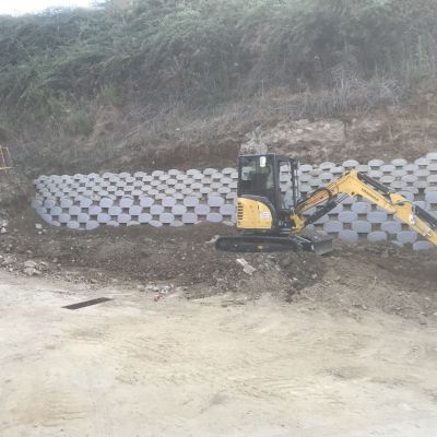 Un escavatore giallo sta lavorando su un muro di cemento.
