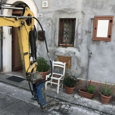 Un escavatore giallo è parcheggiato davanti a un edificio con il numero 12