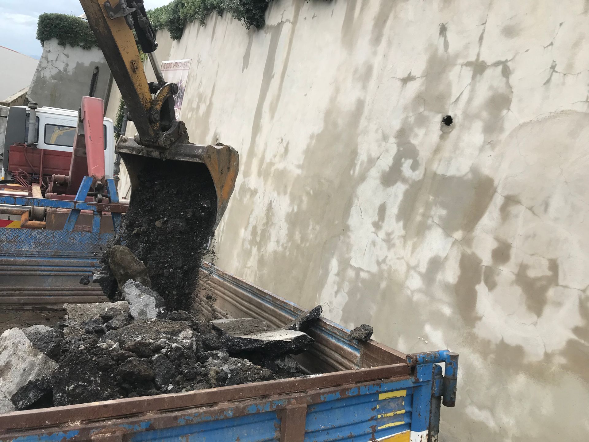 Un escavatore sta caricando terra in un cassonetto.