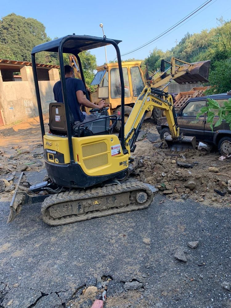 Un uomo sta guidando un piccolo escavatore giallo su una strada sterrata.