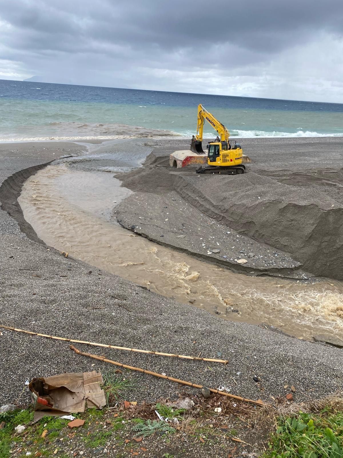 Un escavatore giallo sta lavorando su una spiaggia vicino all'oceano.