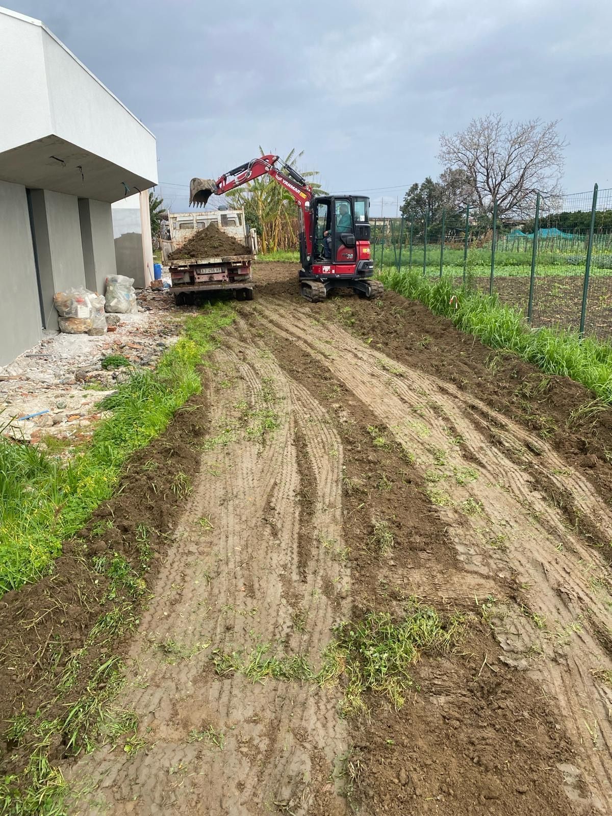 Un escavatore rosso sta percorrendo una strada sterrata accanto a una casa.
