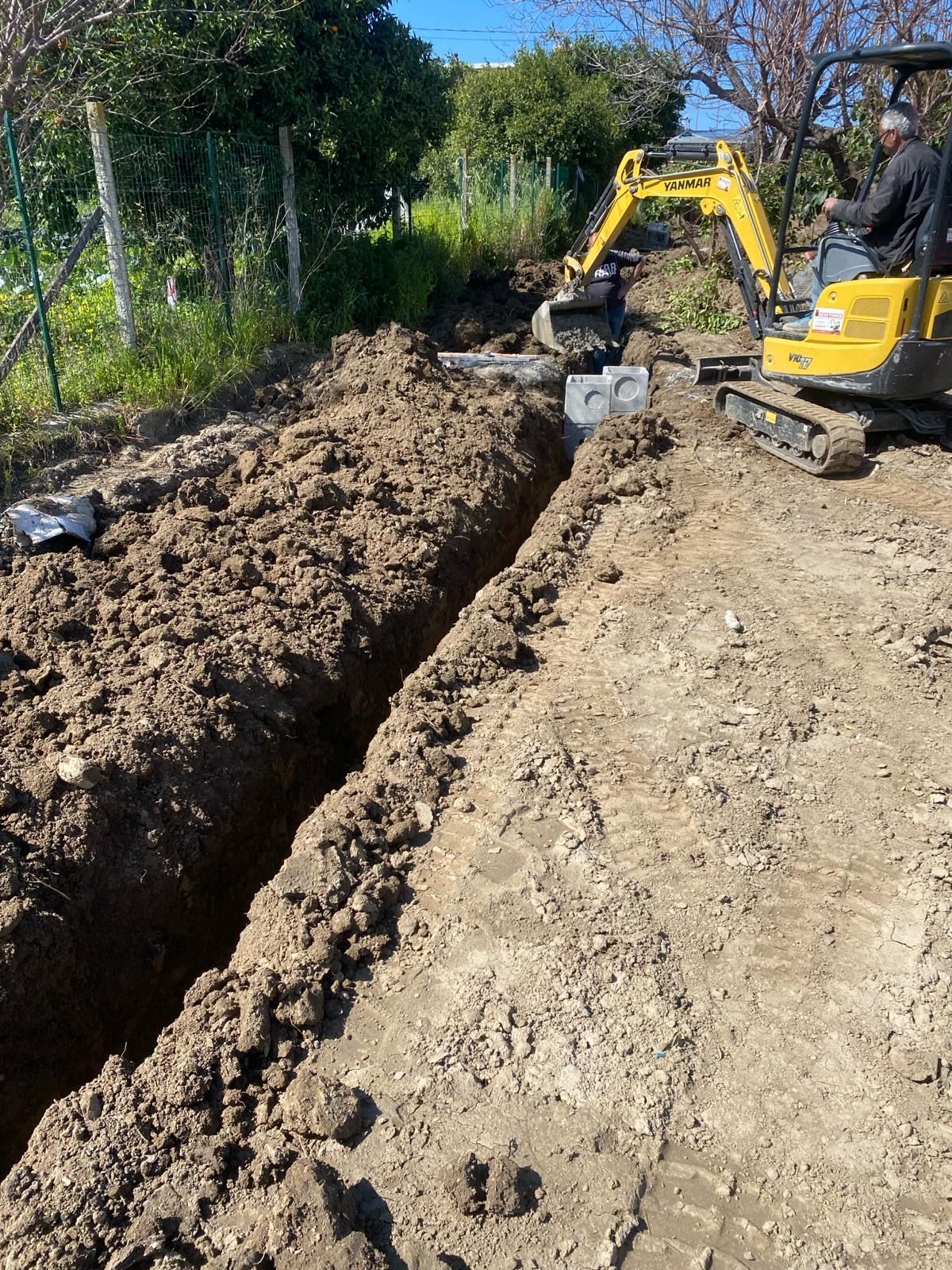 Un escavatore giallo sta scavando una trincea nel terreno.