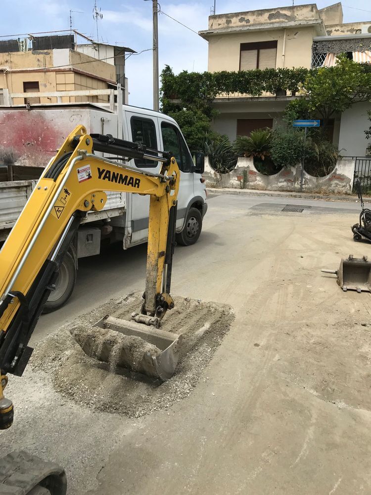 Un escavatore giallo è parcheggiato sul ciglio della strada accanto a un furgone bianco.