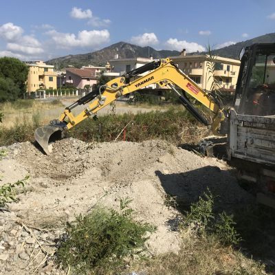 Un escavatore giallo sta scavando una buca in un campo accanto a un camion.
