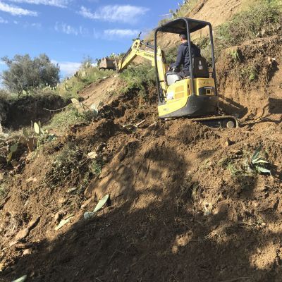 Un uomo sta guidando un piccolo escavatore lungo una collina sterrata.