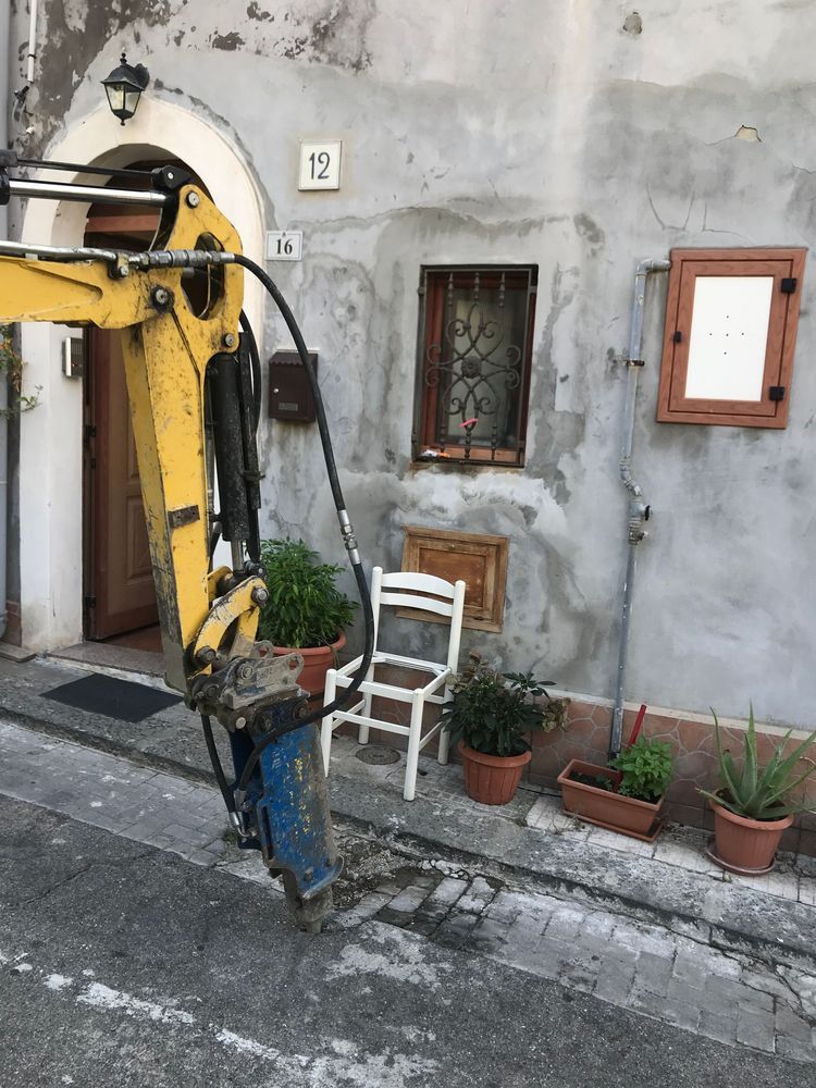 Un escavatore giallo sta scavando una buca davanti a un edificio.
