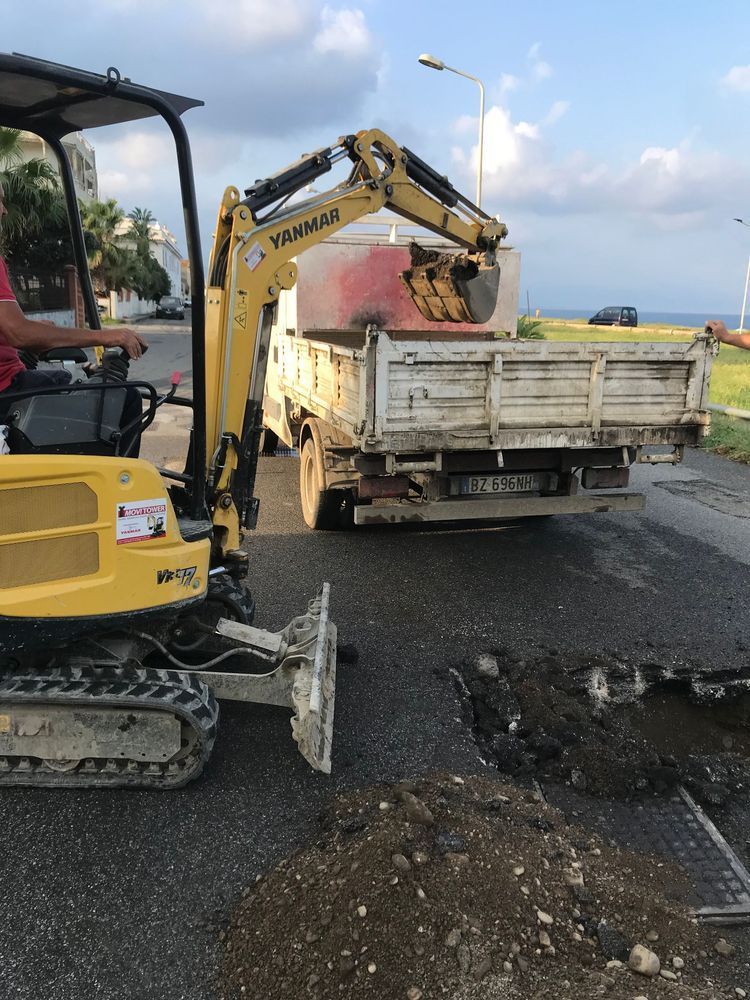 Un escavatore giallo sta scavando una buca nel terreno accanto a un camion.