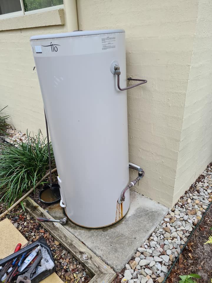 Gray Water Heater Tank Mounted on Concrete Pad Next to a Light Beige Wall — 24/7 Hot Water in Valdora, QLD