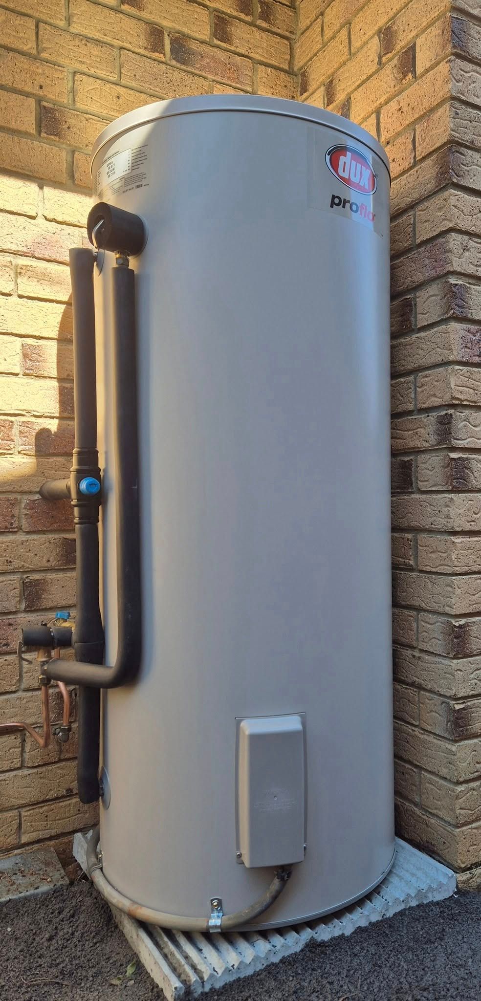 A Tall, Cylindrical Water Heater Against a Brick Wall — 24/7 Hot Water in Valdora, QLD