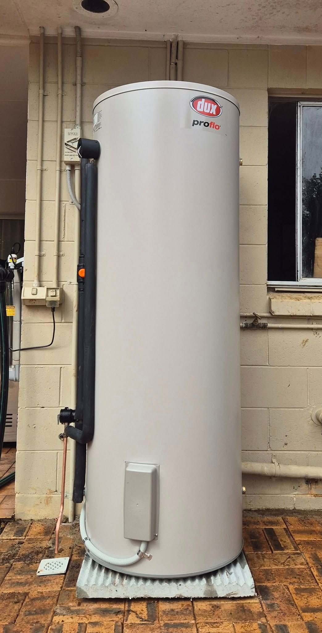 Tall, Cylindrical, Beige Hot Water Heater Against a Beige Building Wall — 24/7 Hot Water in Valdora, QLD
