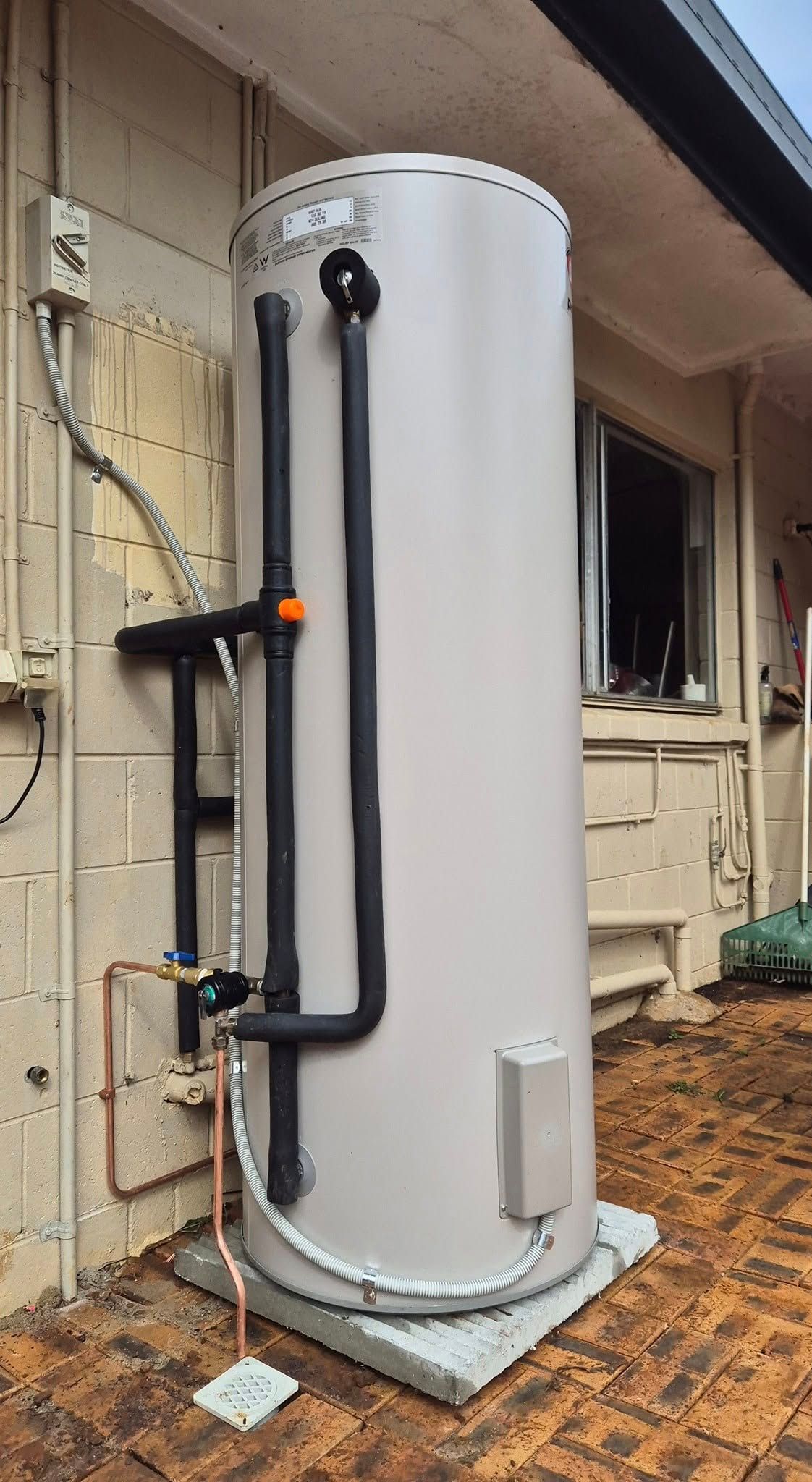 A Tall, Gray Water Heater Tank Installed on a Concrete Base Next to a Light-colored Wall — 24/7 Hot Water in Valdora, QLD