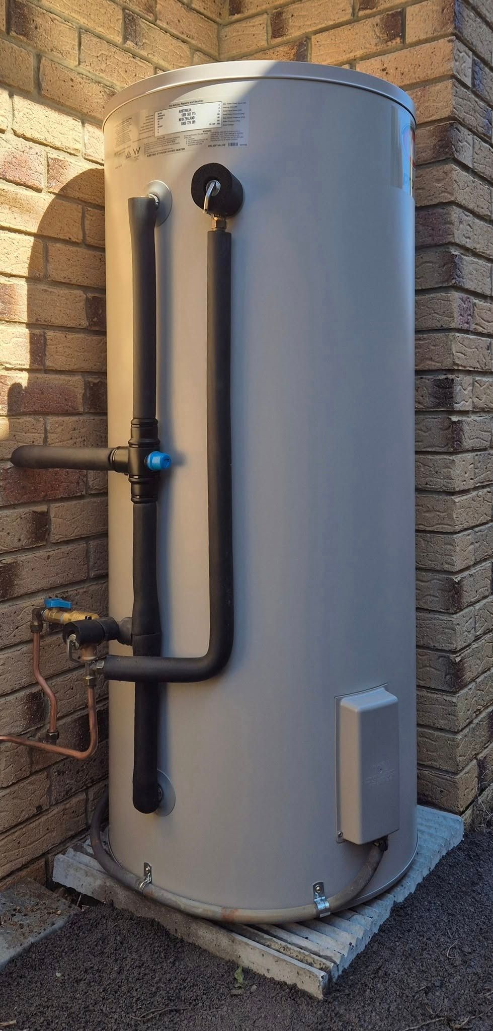 A Tall, Cylindrical, Gray Water Heater Next to a Brick Wall — 24/7 Hot Water in Maroochydore, QLD