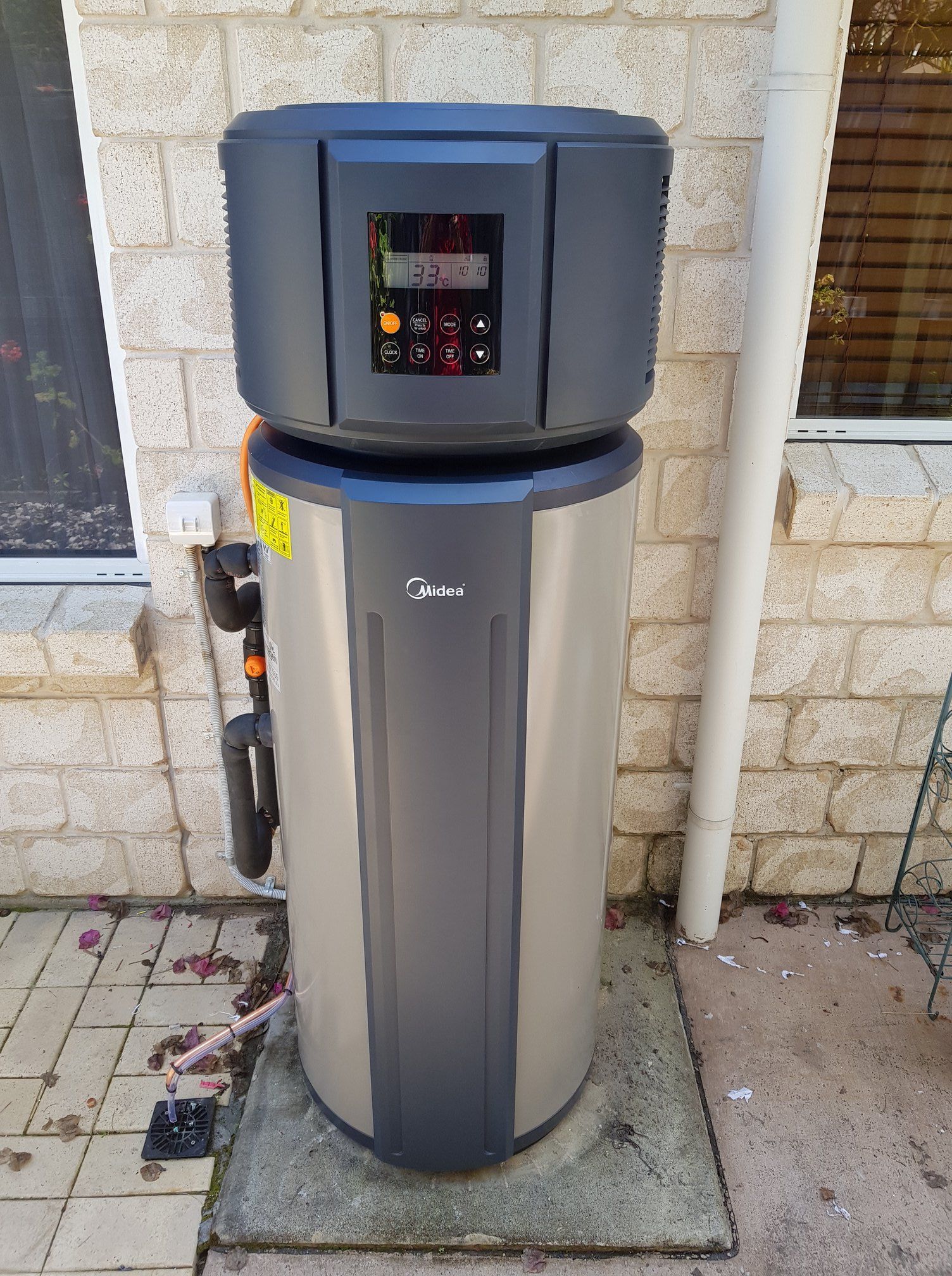 A Tall, Silver and Gray Electric Hot Water Heater Outside Against a Brick Wall — 24/7 Hot Water in Gympie, QLD