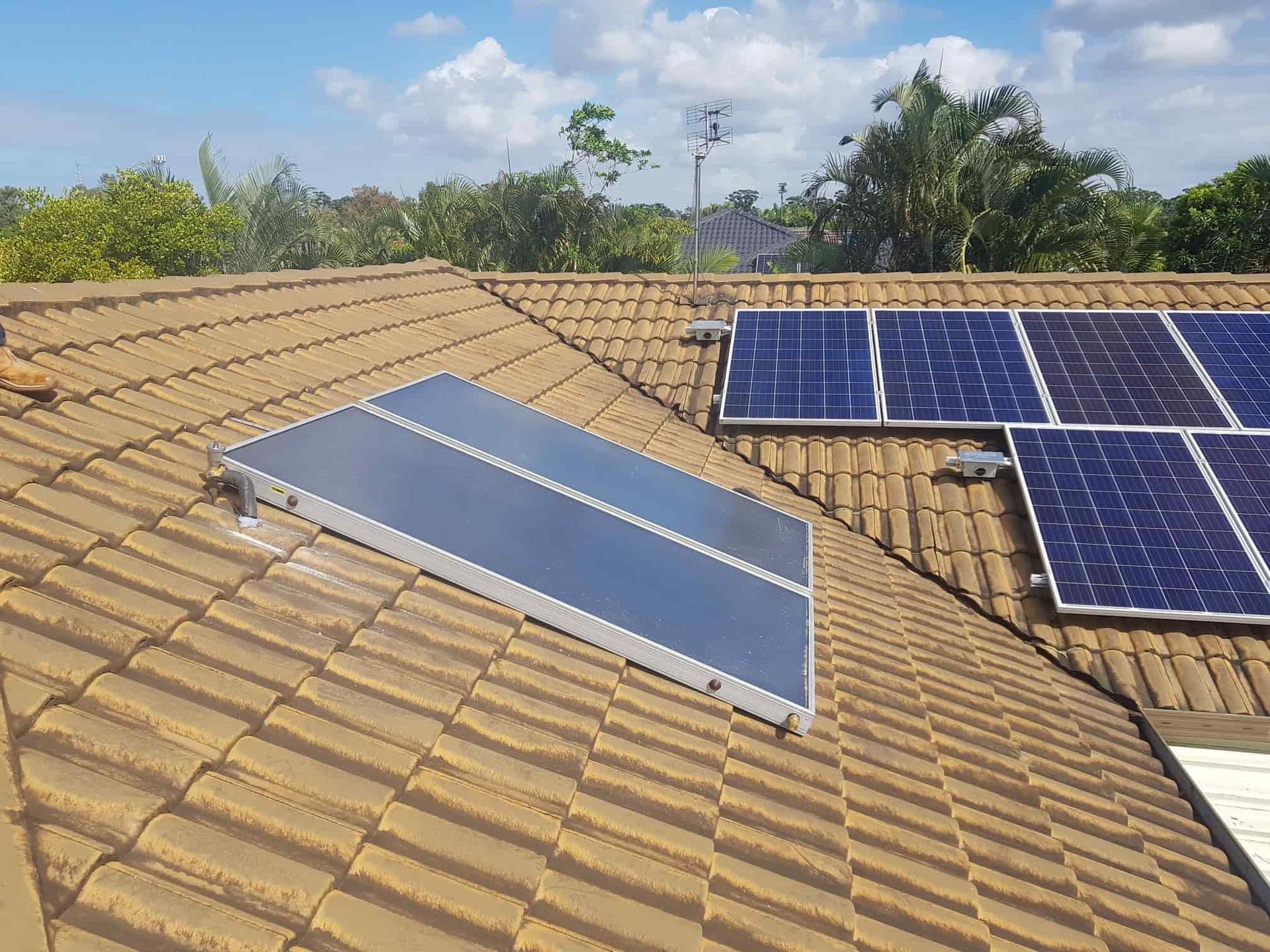 Solar panels mounted on a brown tiled roof under a partly cloudy blue sky. — 24/7 Hot Water in Gympie, QLD