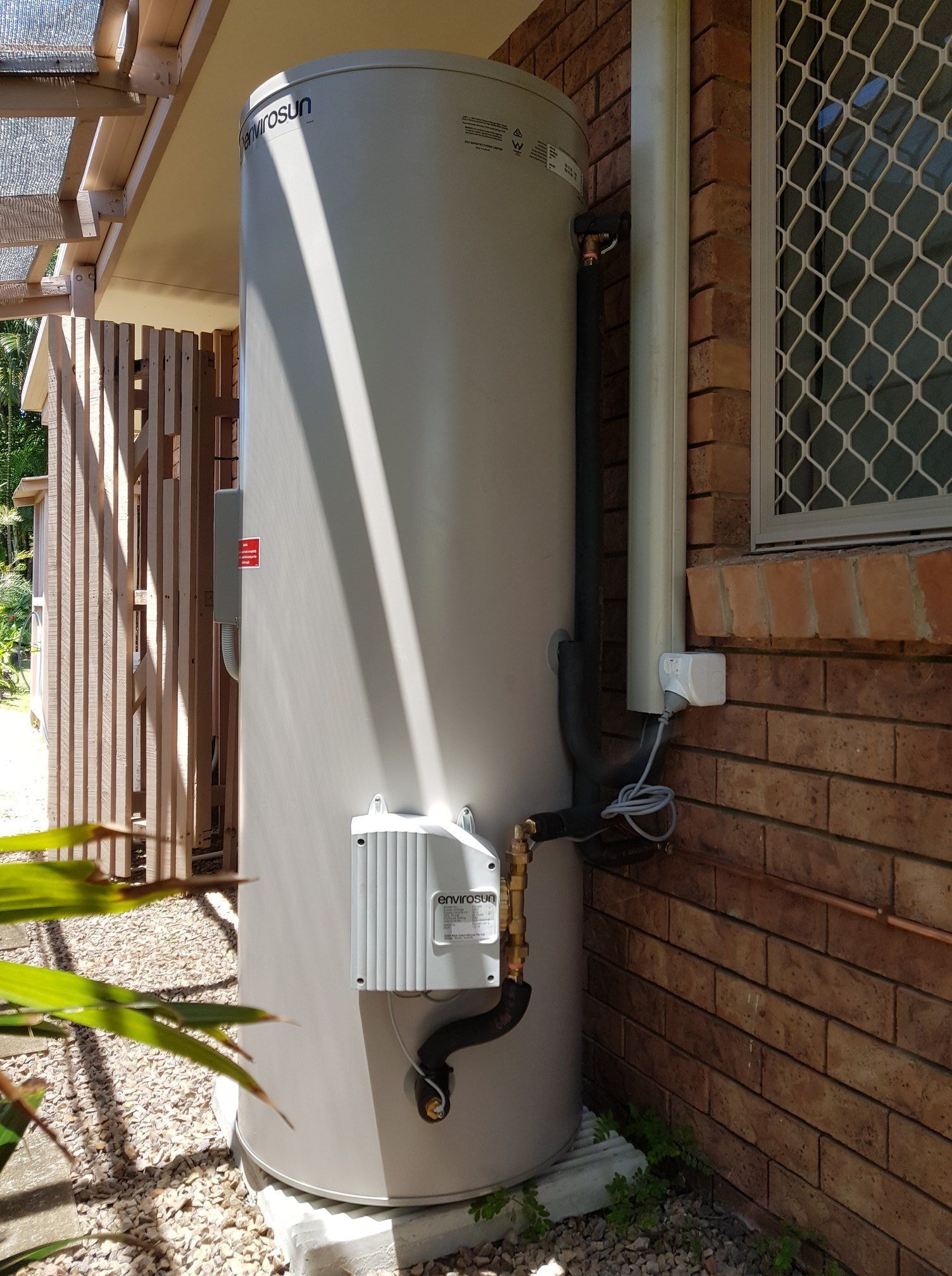 A tall, grey hot water heater next to a brick wall with black and silver piping. — 24/7 Hot Water in Gympie, QLD