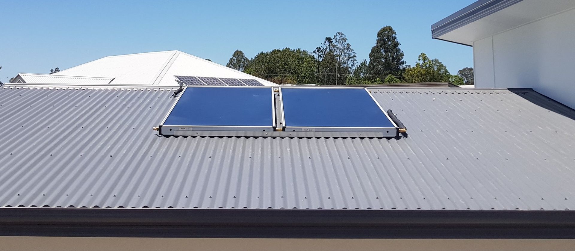 Two Solar Panels on a Gray Corrugated Metal Roof Under a Blue Sky — 24/7 Hot Water in Maroochydore, QLD
