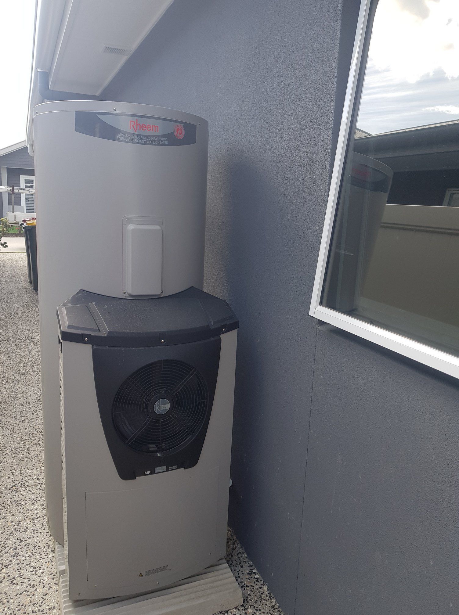 Gray Heat Pump and Water Heater Unit Next to a Gray Building Wall — 24/7 Hot Water in Caloundra, QLD